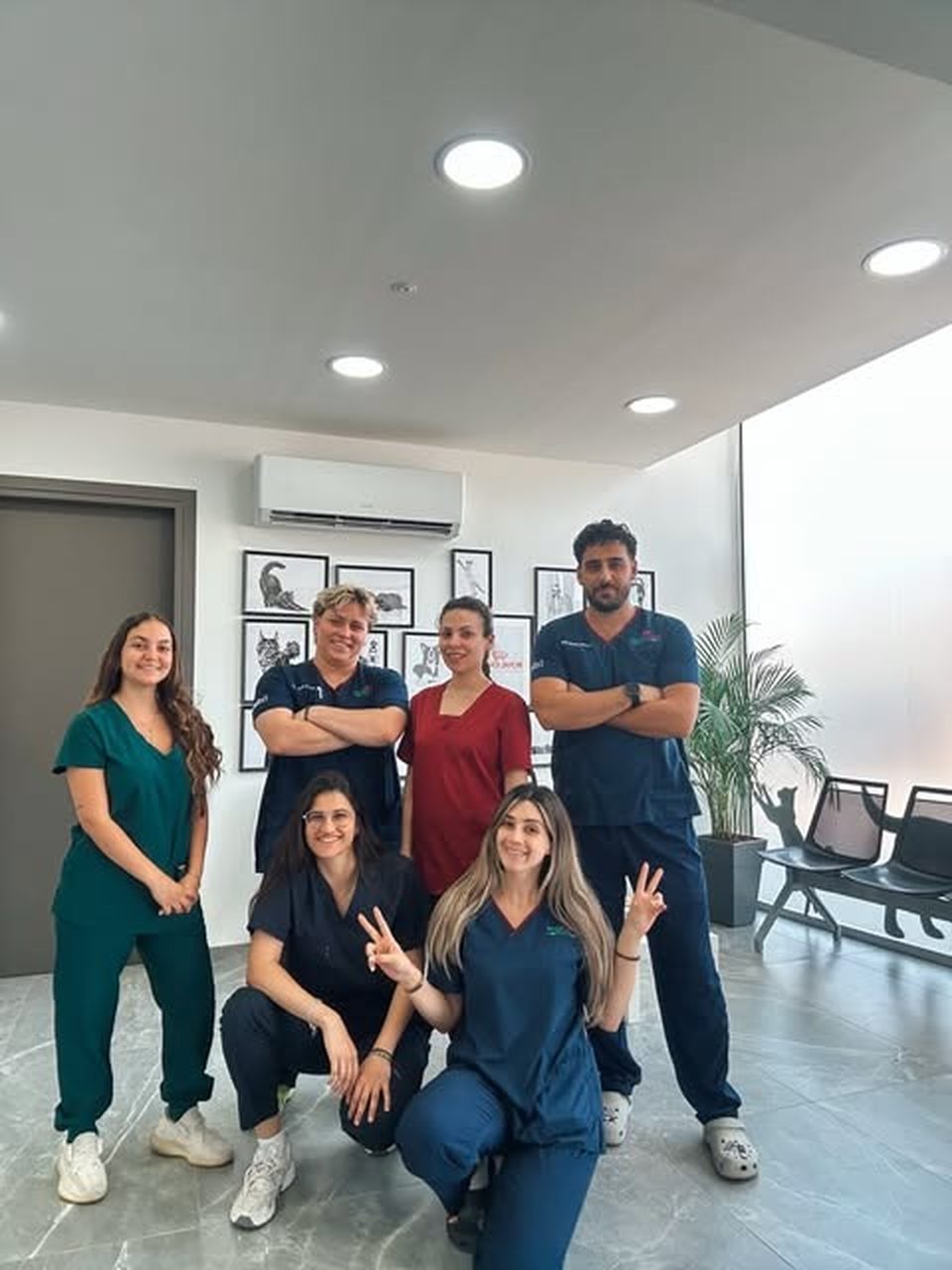 Seven people in navy, green and burgundy scrubs posing together in the clinic's waiting area: the team with veterinary students from Trakia University who trained at the clinic in summer 2026